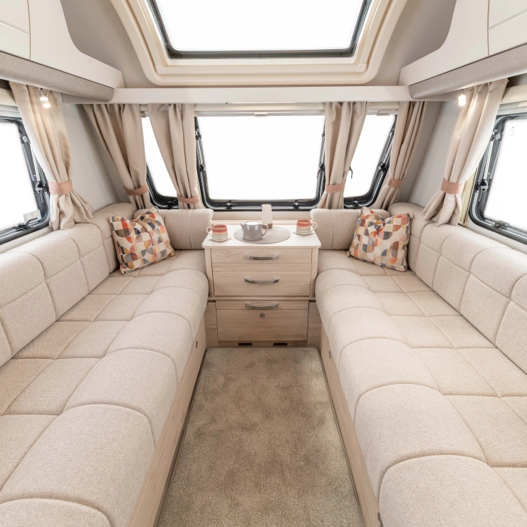 A closer interior image of the Elddis Whirlwind 520. It shows the lounge area with seating on both side of the caravan and windows surrounding it.