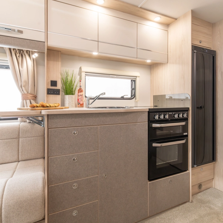 This picture shows the kitchen area inside the Elddis Whirlwind 520. You can see the cooker and grill alongside the sink towards the left, lighting and cupboards above with a fridge towards the right hand side of the kitchen unit.