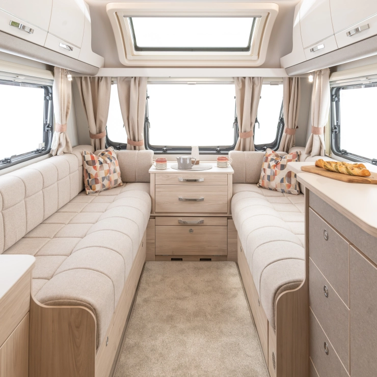 An interior image of the Elddis Whirlwind 520. It shows the lounge area with seating on both side of the caravan and windows surrounding it.