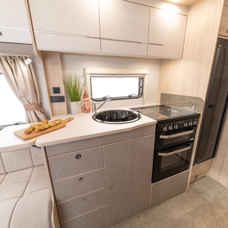 Top angle view of the kitchen area inside the Elddis Whirlwind 520. You can see the cooker and grill alongside the sink towards the left, lighting and cupboards above with a fridge towards the right hand side of the kitchen unit.